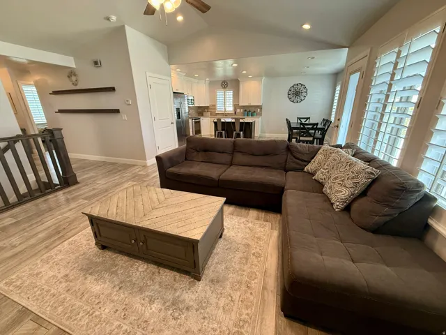Open-concept living space featuring vaulted ceilings, wood-finish flooring, a ceiling fan, and plantation shutters