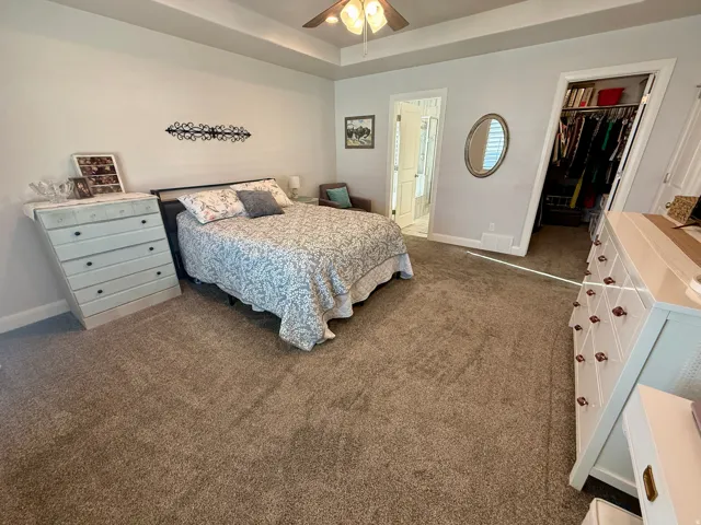 Spacious bedroom featuring neutral carpeting, a tray ceiling, and a ceiling fan