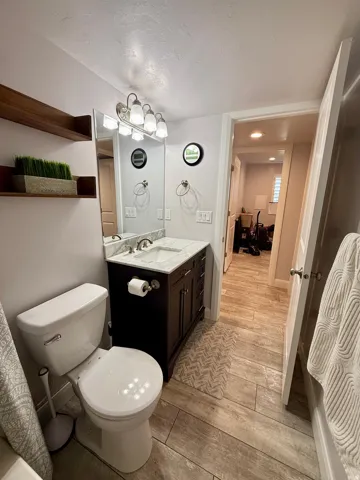 Bathroom vanity featuring a single basin sink set in a light-toned countertop, a dark wood-finish cabinet with storage, a wall-mounted mirror, and a five-light fixture