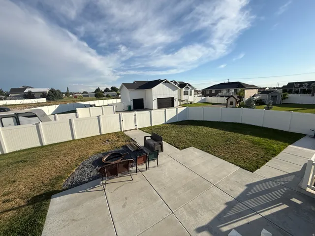 Spacious backyard featuring a large concrete patio, a section of manicured lawn, and a white privacy fence enclosing the property