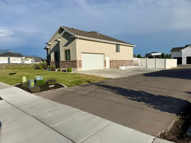 Contemporary residence featuring a two-car garage, partial stone facade, and a vinyl privacy fence enclosing a concrete patio