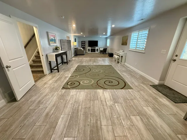 Spacious lower-level area featuring wood-finish flooring, recessed lighting, white window shutters, and a carpeted stairway entry