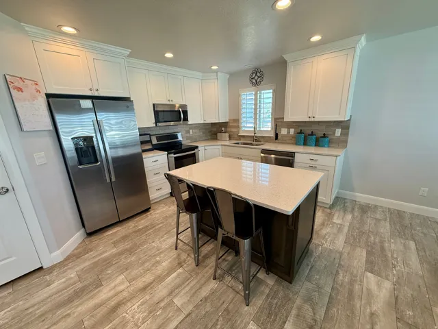Kitchen featuring a central island with countertop seating, stainless steel appliances, white cabinetry, wood-finish flooring, and a tile backsplash