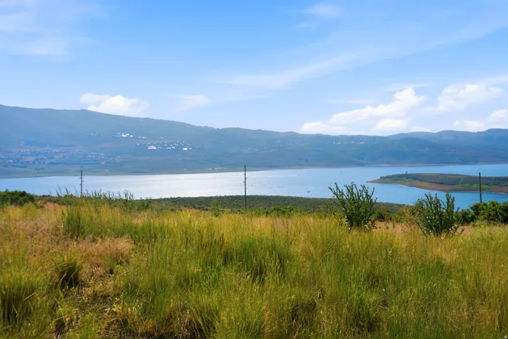 Expansive natural landscape featuring a prominent body of water, distant mountain range, and a clear blue sky