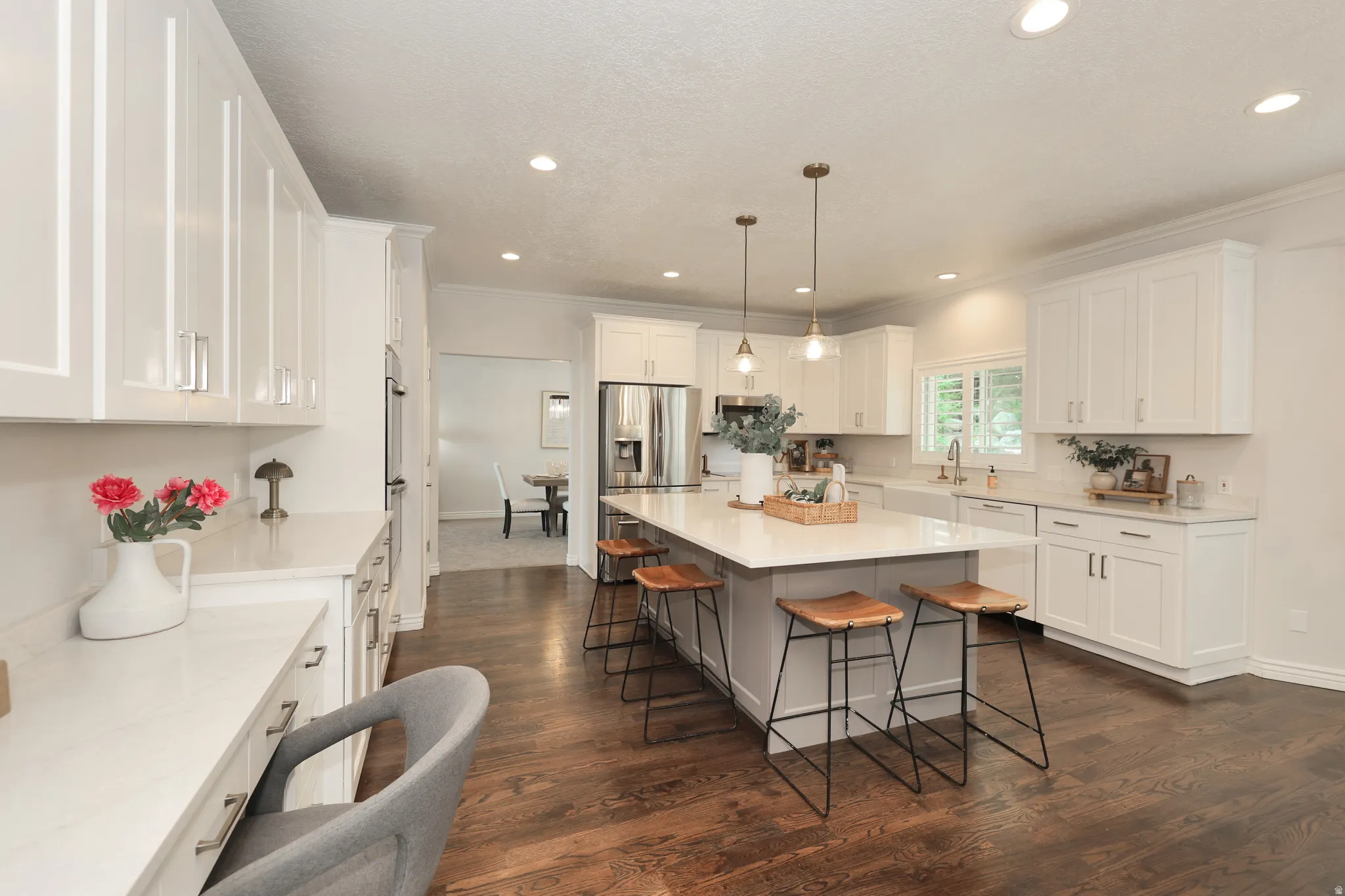 Spacious kitchen featuring an expansive center island with pendant lighting, white shaker cabinetry, stainless steel appliances, white countertops, and wood-finish flooring