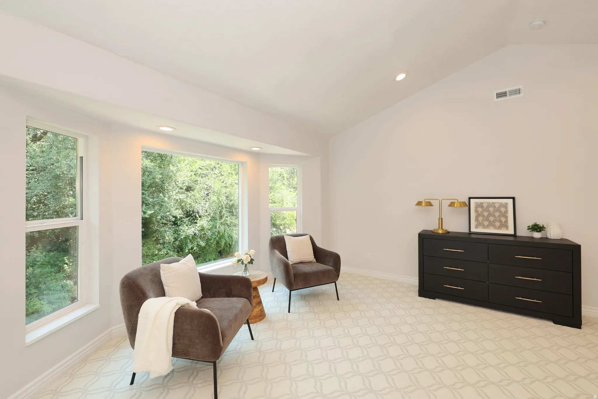 Bright room featuring multiple windows with tree-lined scenery, a vaulted ceiling, recessed lighting, and patterned carpeting