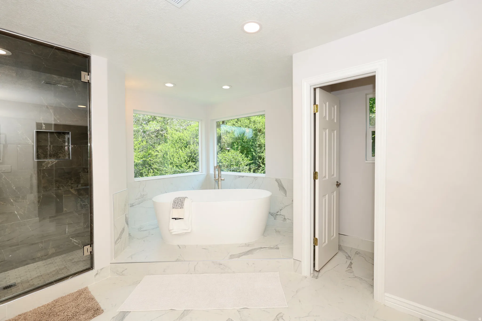 Freestanding soaking tub with floor-mounted faucet set on a tiled platform, surrounded by expansive windows