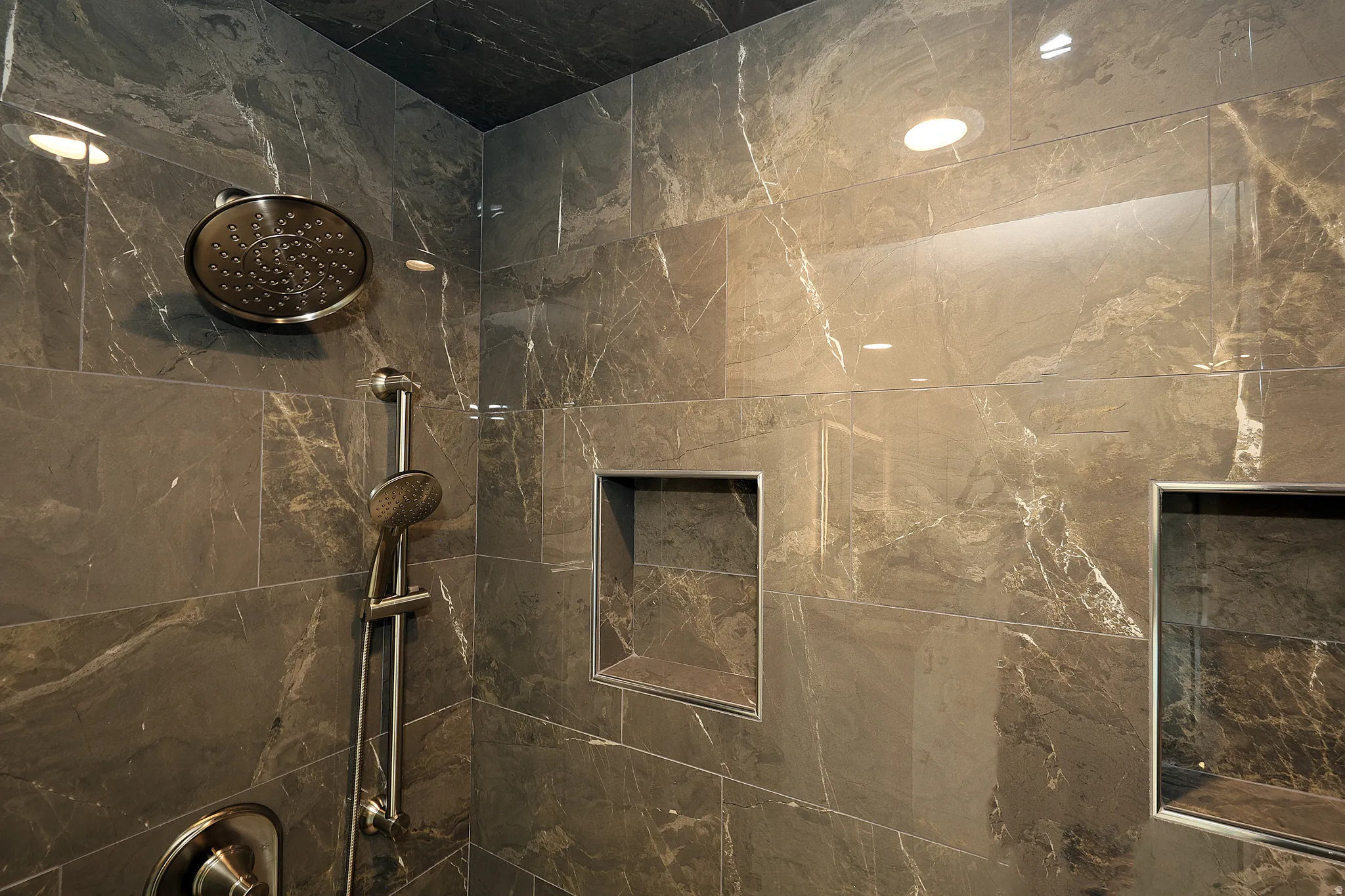 Shower stall featuring large format marbled tile, a rainfall showerhead, and a handheld shower wand
