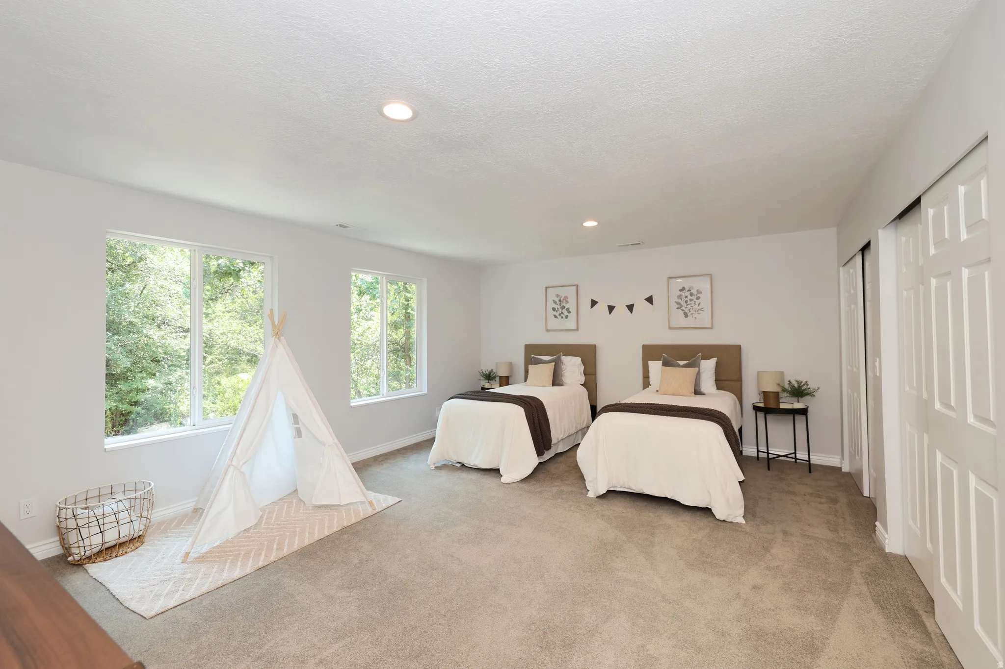 Spacious room featuring light gray wall paint and two large windows offering verdant exterior views