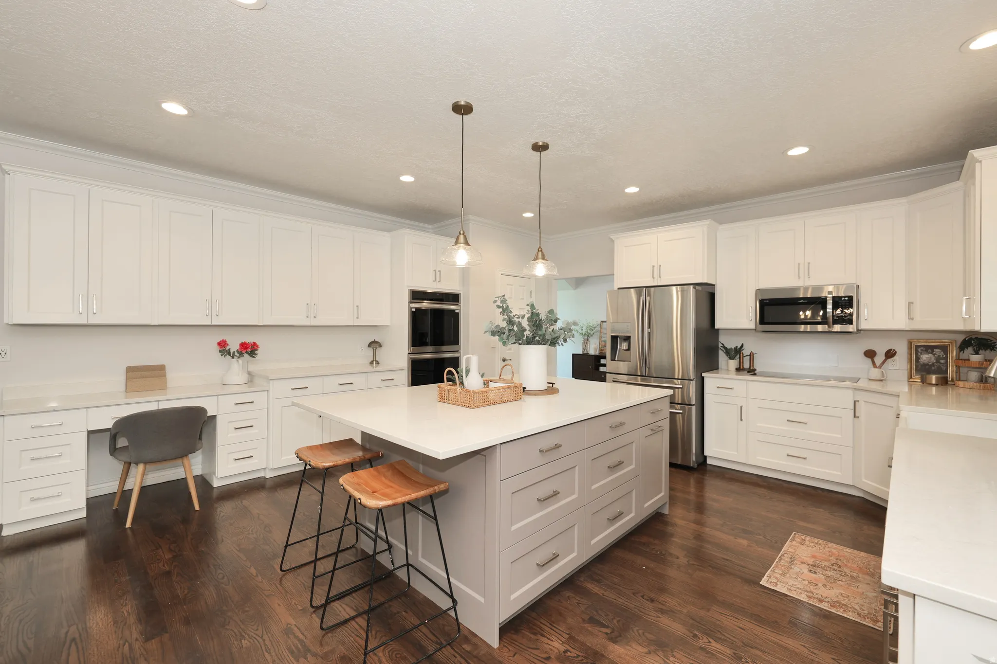 Modern kitchen featuring a large central island with seating, extensive white cabinetry, light-toned countertops, dark wood-finish flooring, and recessed lighting