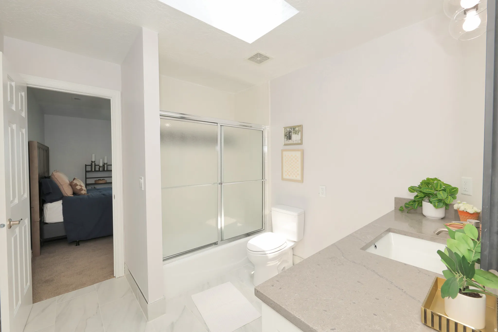 Bathroom featuring a skylight, white tiled flooring, a shower with frosted sliding glass doors, a vanity with a rectangular undermount sink, and a stone-finish countertop