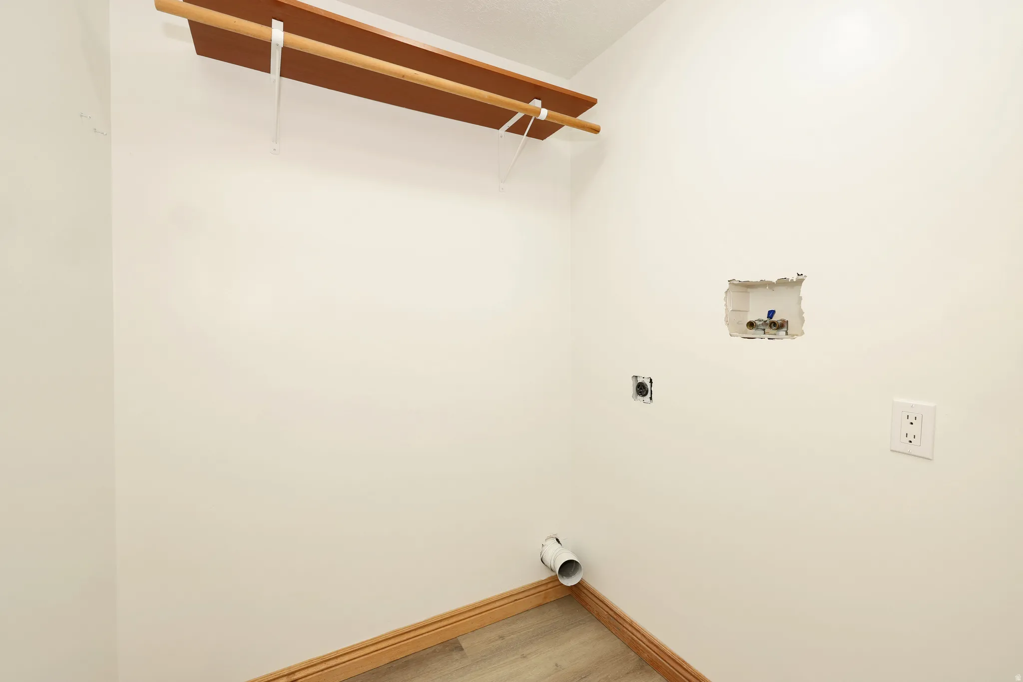 Laundry area featuring a wood-finish shelf with a hanging rod, wall-mounted electrical outlets, and plumbing hookups