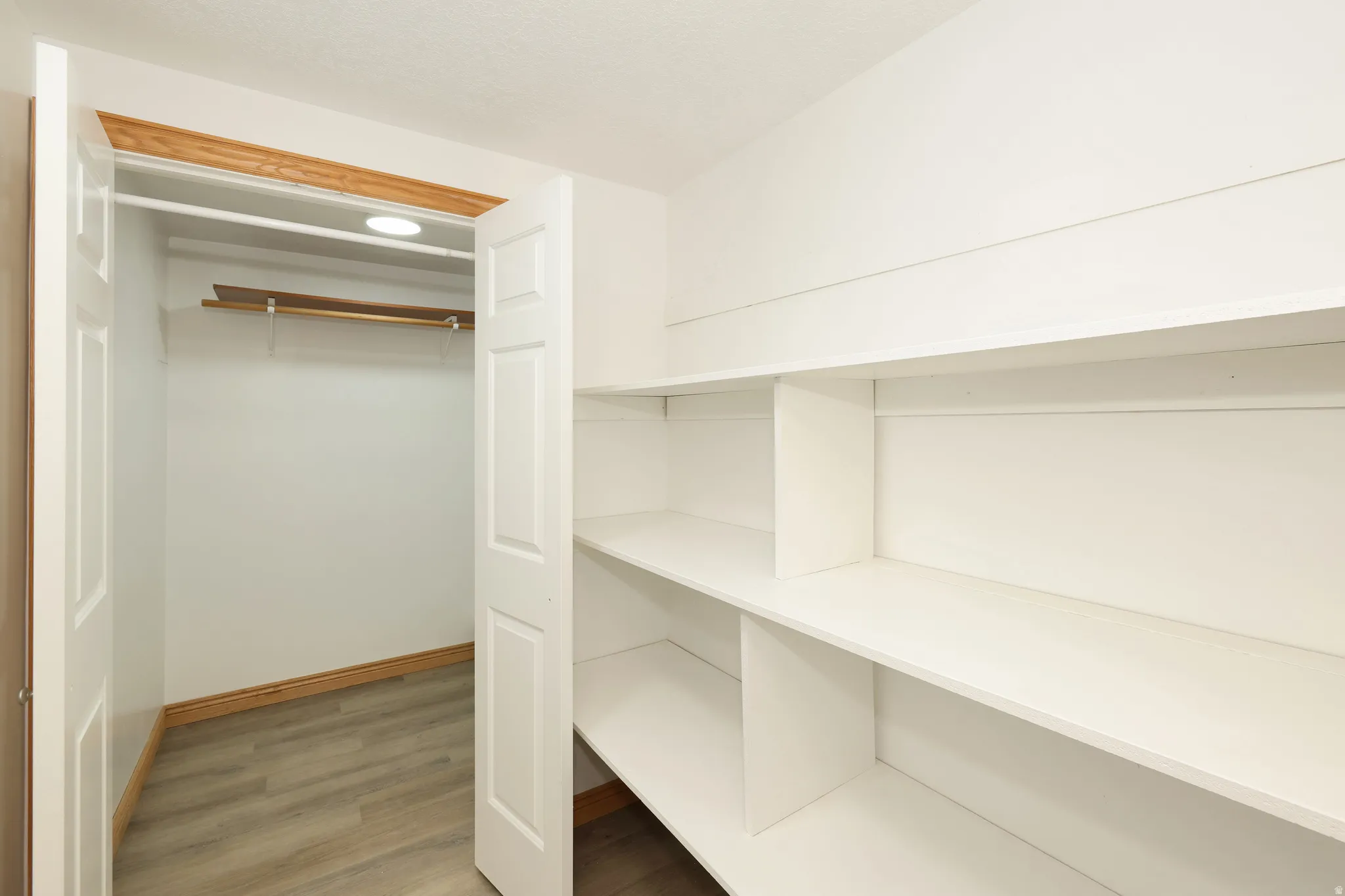 Bright white pantry and storage area featuring built-in shelving, wood-finish flooring, and a recessed ceiling light