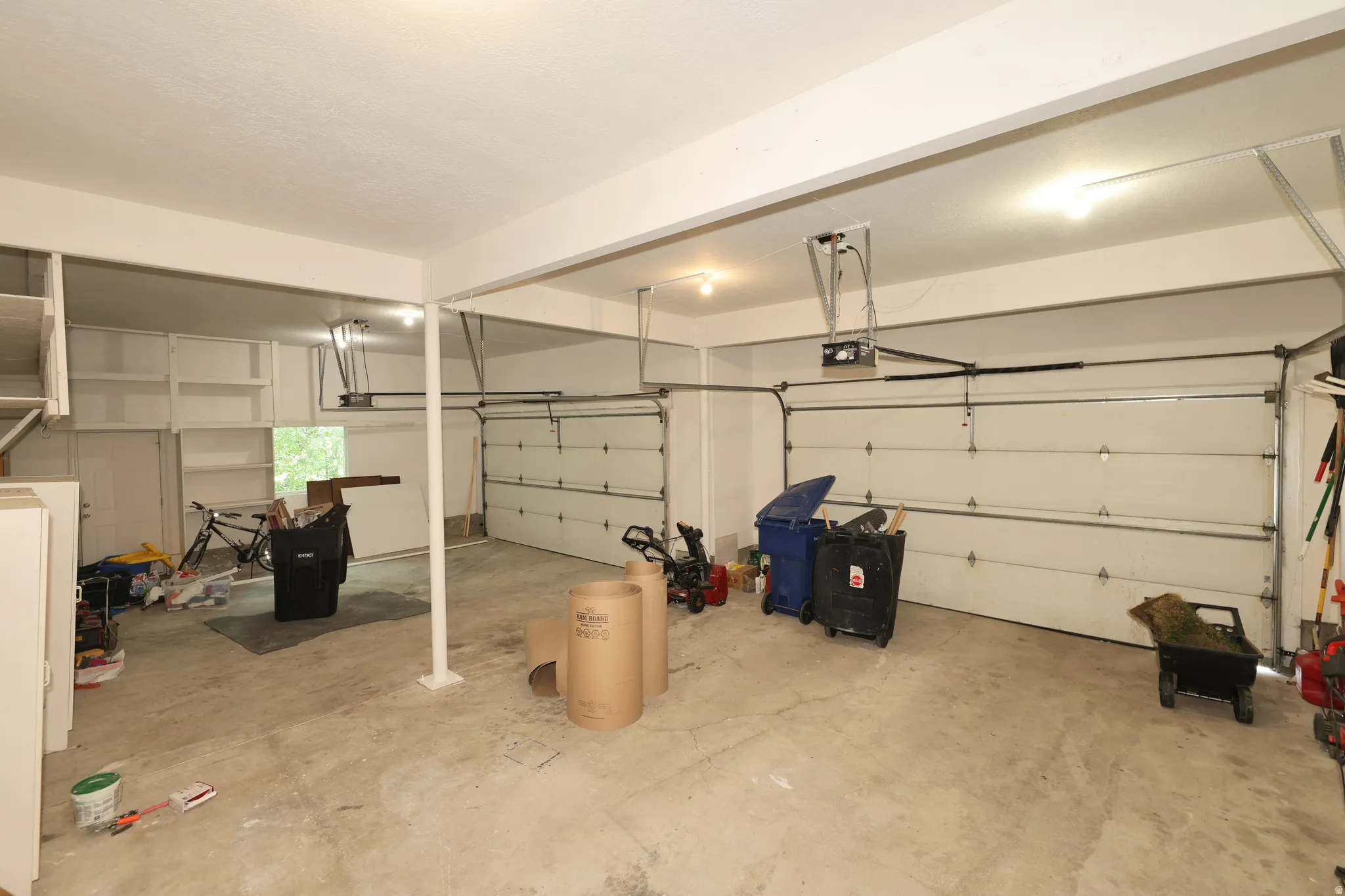 Spacious garage featuring two overhead doors, exposed support beams, built-in shelving, and a concrete floor