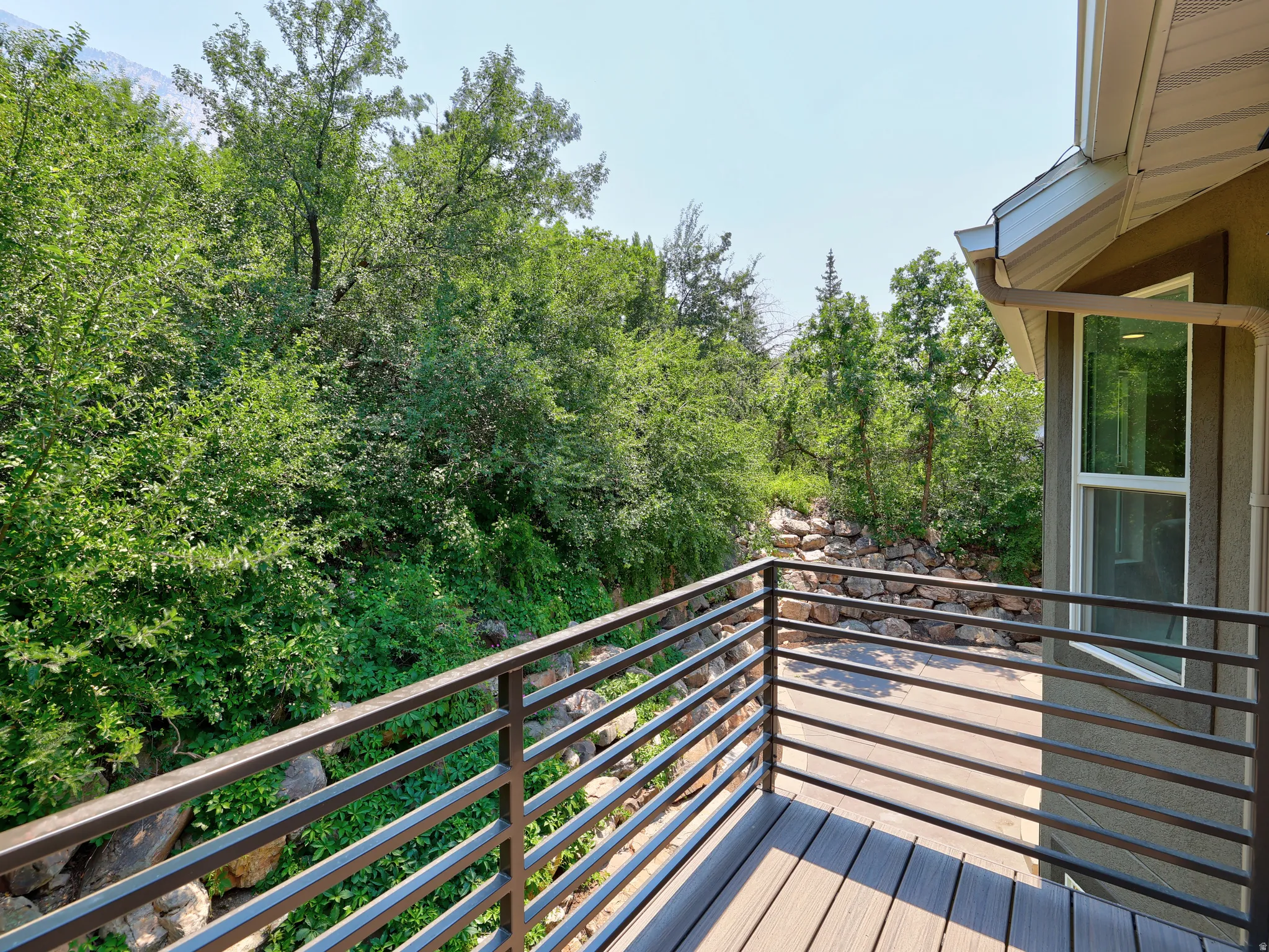 Outdoor deck featuring composite decking, horizontal metal railings, and natural surroundings with mature trees