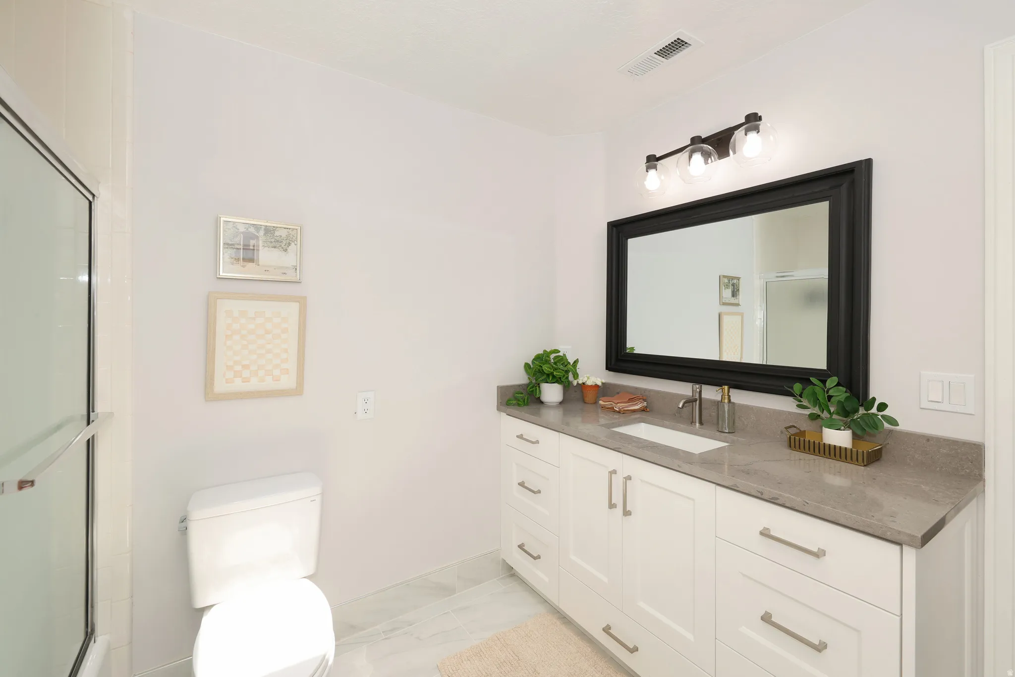 Modern bathroom featuring a single vanity with stone countertop, undermount sink, and matte black framed mirror with a three-light fixture