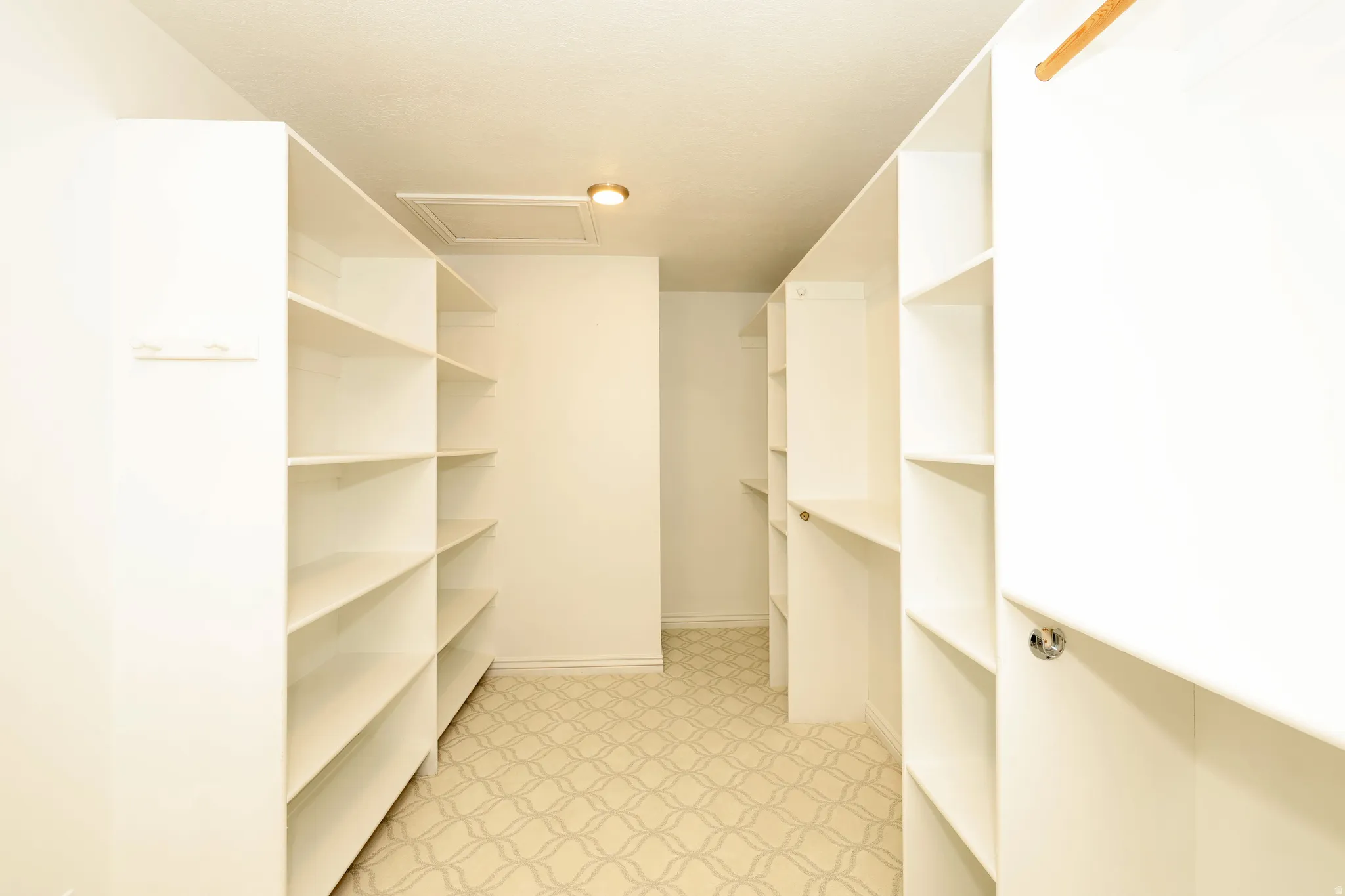 Spacious walk-in closet featuring extensive built-in shelving, a natural wood-finish hanging rod, and patterned carpet flooring