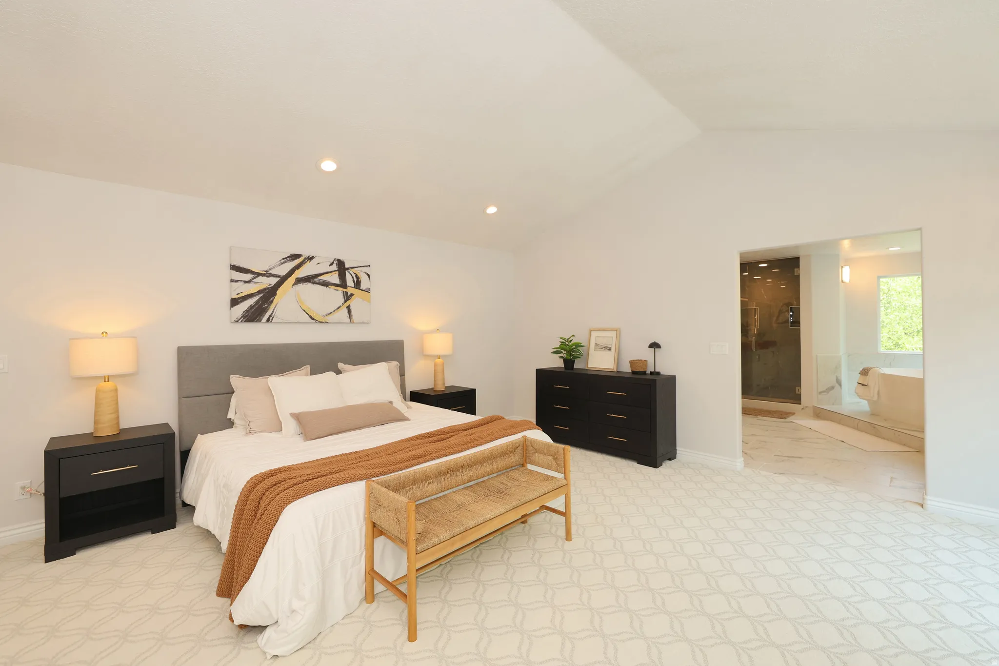 Spacious bedroom featuring vaulted ceilings, patterned carpeting, recessed lighting, and direct access to an ensuite bathroom with a glass-enclosed shower and soaking tub