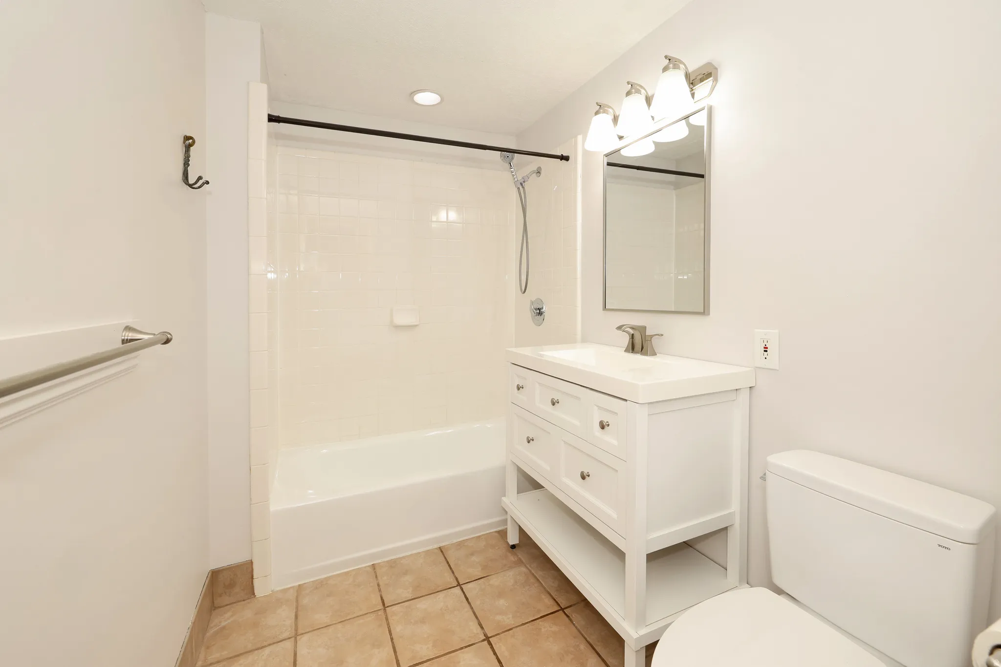 Bathroom featuring a white vanity with an integrated sink, brushed nickel faucet, and a mirror with a three-light fixture
