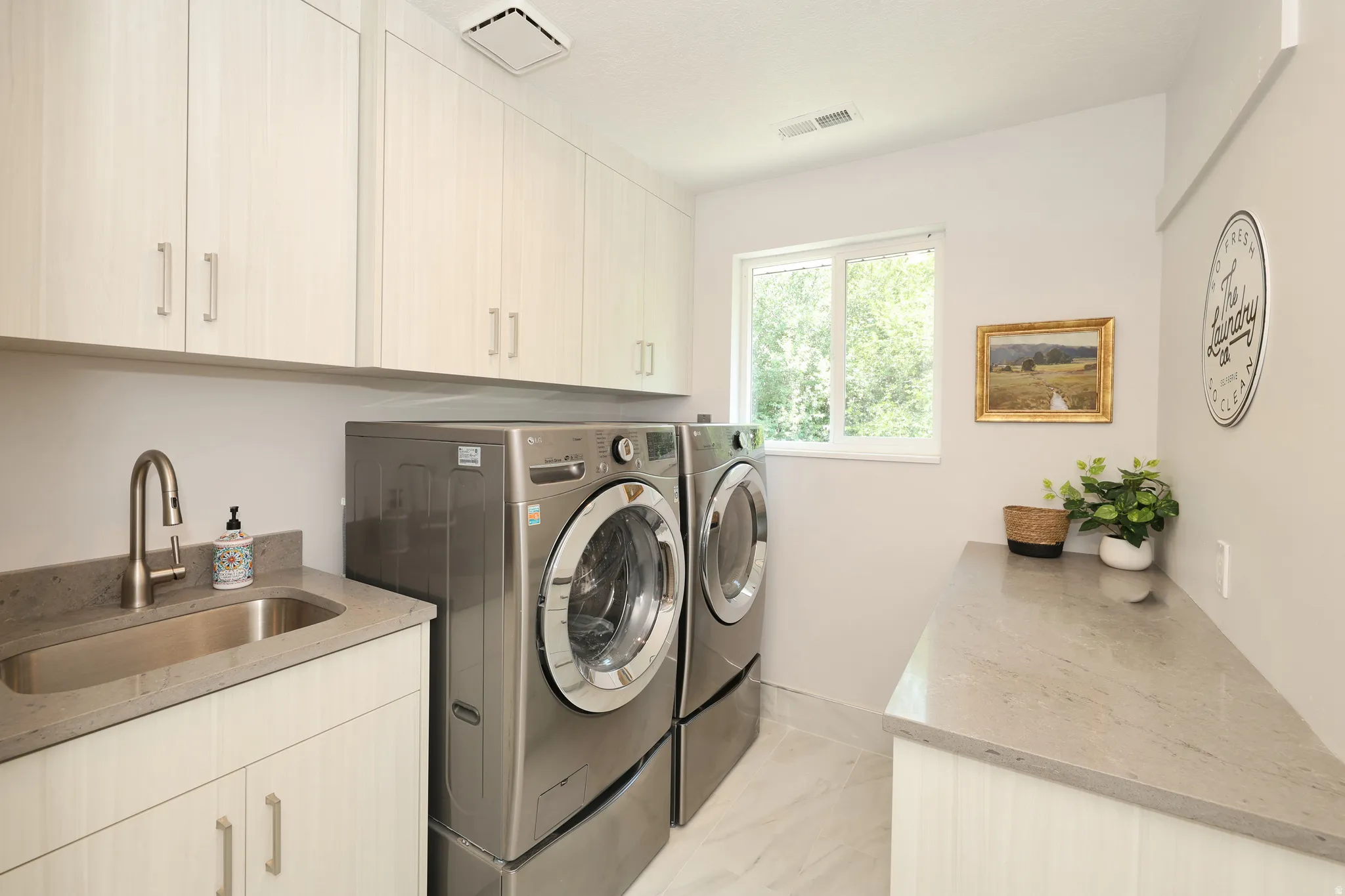 Dedicated laundry space featuring extensive upper and lower cabinetry, a built-in sink with a brushed nickel faucet, durable countertop surfaces, and large format floor tiling