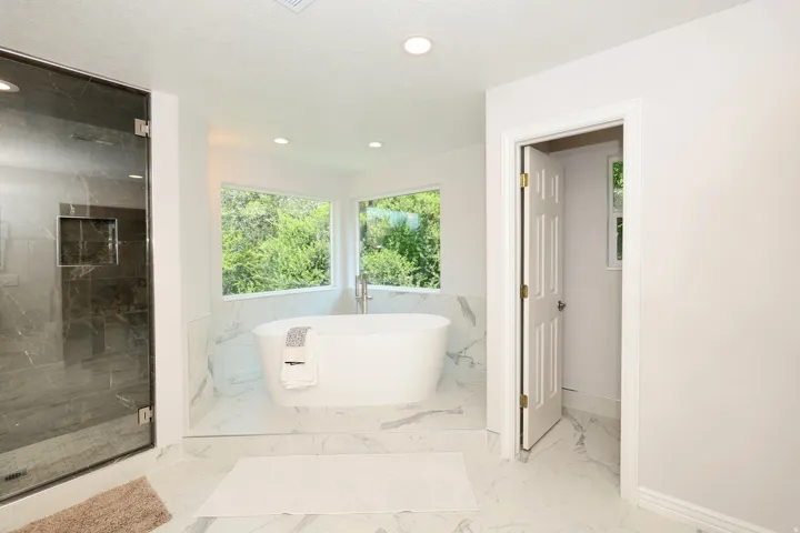 Freestanding soaking tub with floor-mounted faucet set on a tiled platform, surrounded by expansive windows