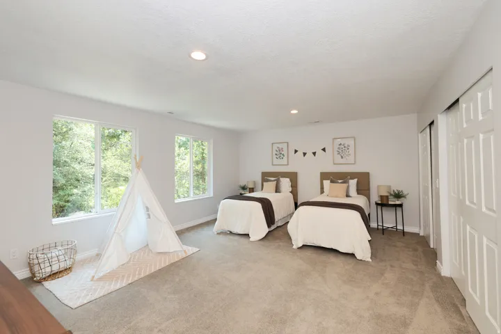 Spacious room featuring light gray wall paint and two large windows offering verdant exterior views