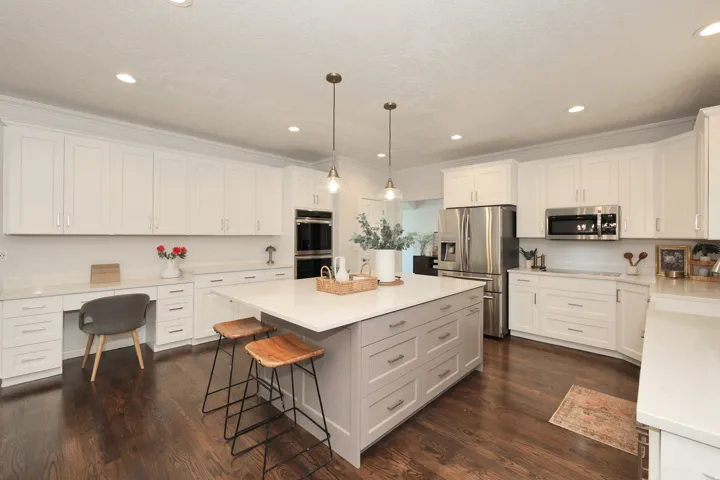 Modern kitchen featuring a large central island with seating, extensive white cabinetry, light-toned countertops, dark wood-finish flooring, and recessed lighting
