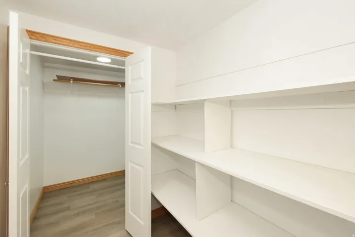 Bright white pantry and storage area featuring built-in shelving, wood-finish flooring, and a recessed ceiling light