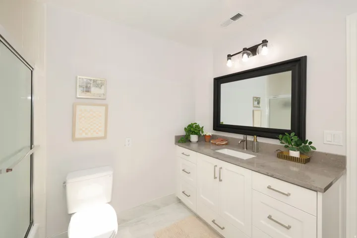 Modern bathroom featuring a single vanity with stone countertop, undermount sink, and matte black framed mirror with a three-light fixture