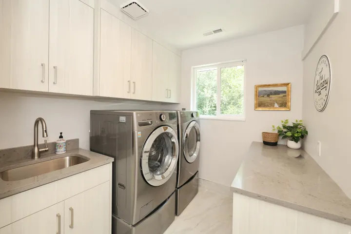 Dedicated laundry space featuring extensive upper and lower cabinetry, a built-in sink with a brushed nickel faucet, durable countertop surfaces, and large format floor tiling