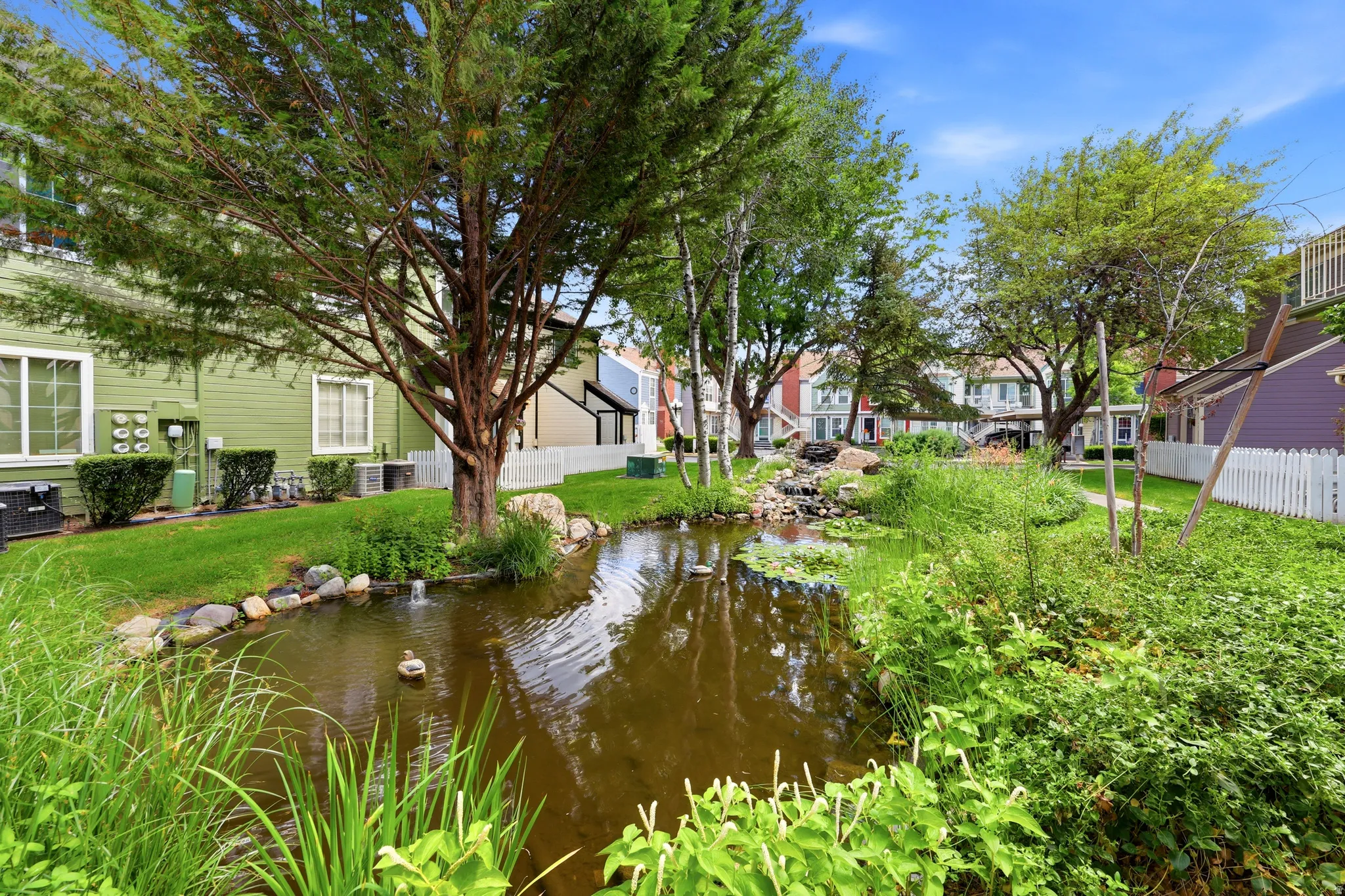 Centrally located water feature with rock accents and a small stream, surrounded by manicured lawns and mature trees