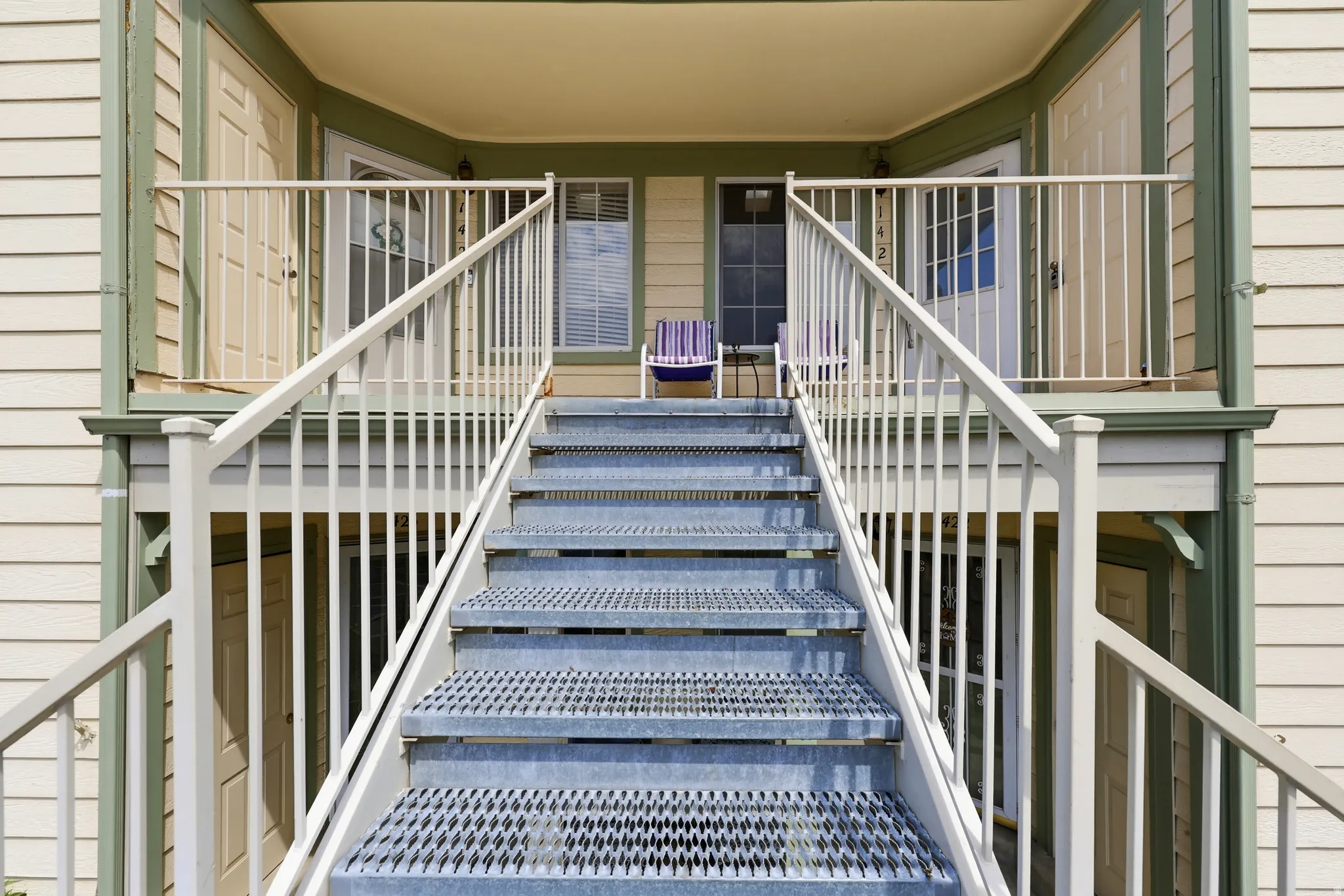 Exterior staircase with metal tread steps and white railings leading to individual unit entrances