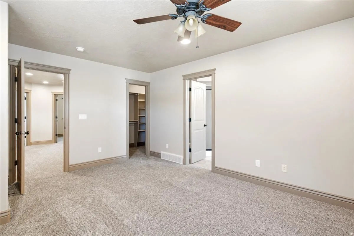 Spacious room featuring light gray walls, plush carpet flooring, and a ceiling fan with light fixture