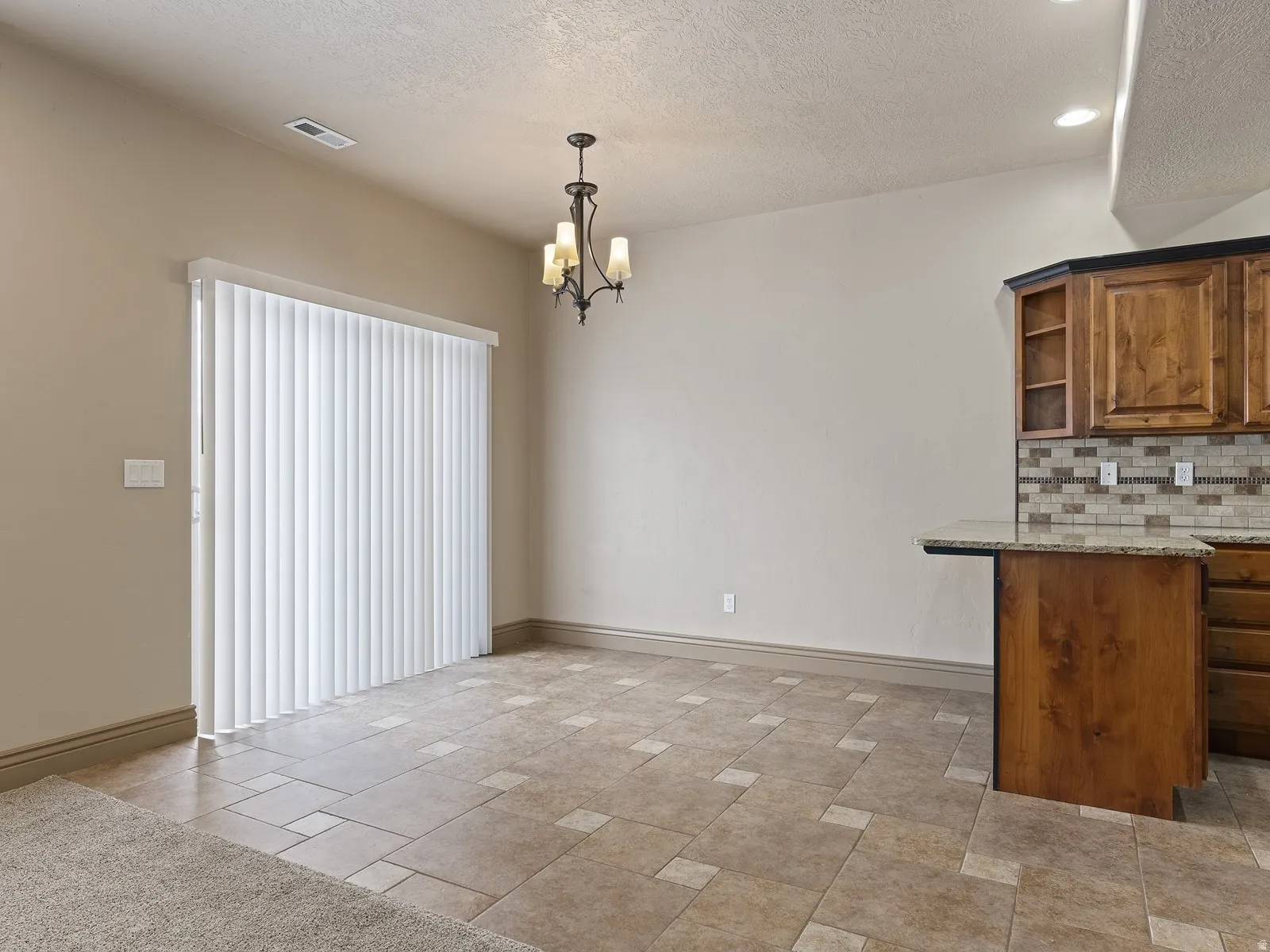 Spacious dining area featuring tile flooring, a multi-paneled sliding glass door with vertical blinds, and a chandelier lighting fixture
