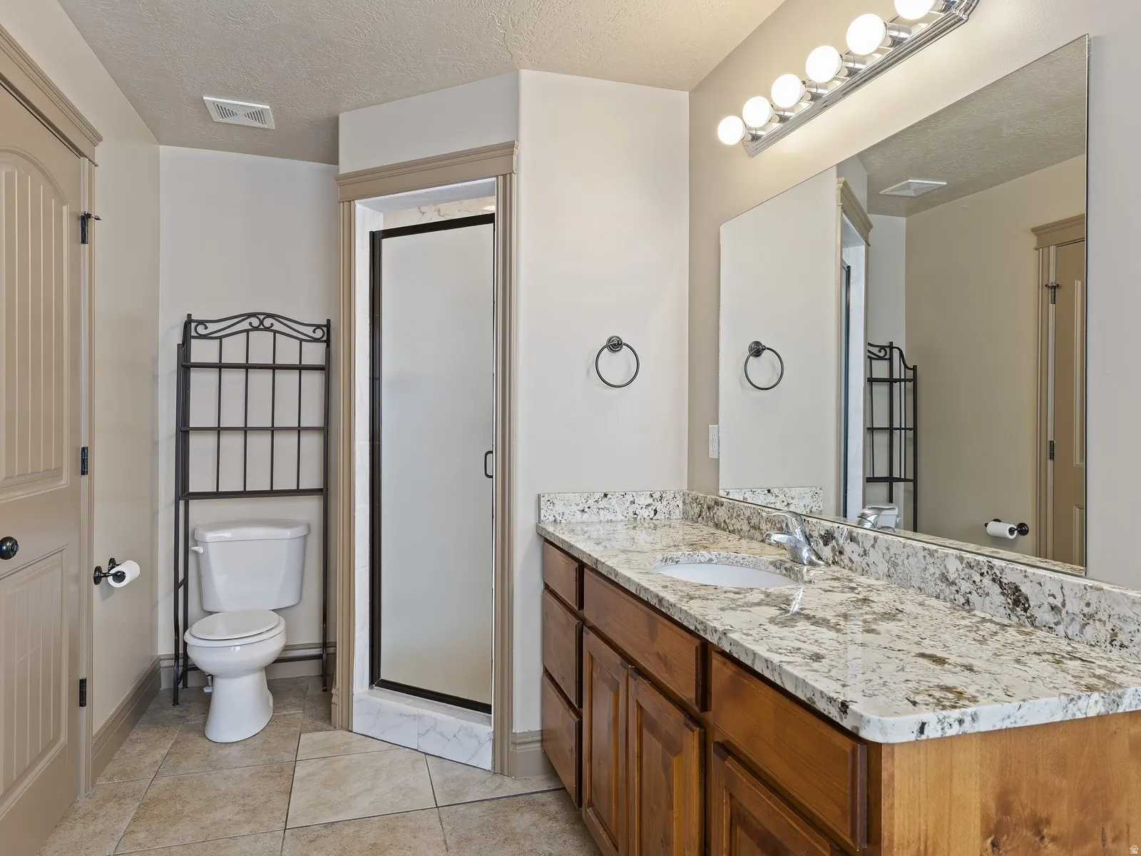 Bathroom featuring a spacious vanity with a granite countertop, undermount sink, and wood cabinetry