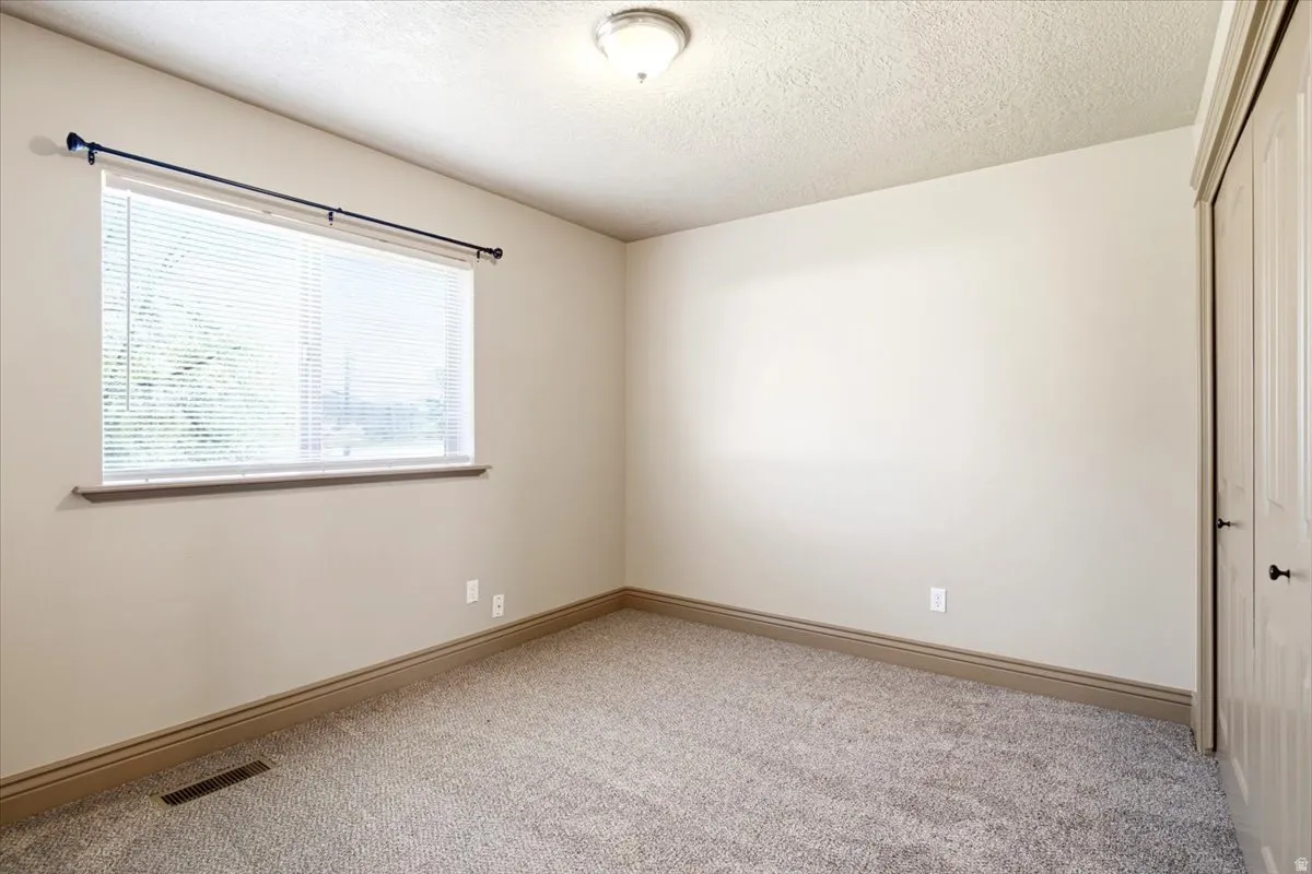 Carpeted interior space featuring a single window with blinds and a dark curtain rod, a flush-mount ceiling light fixture, and a bi-fold closet door with dark hardware