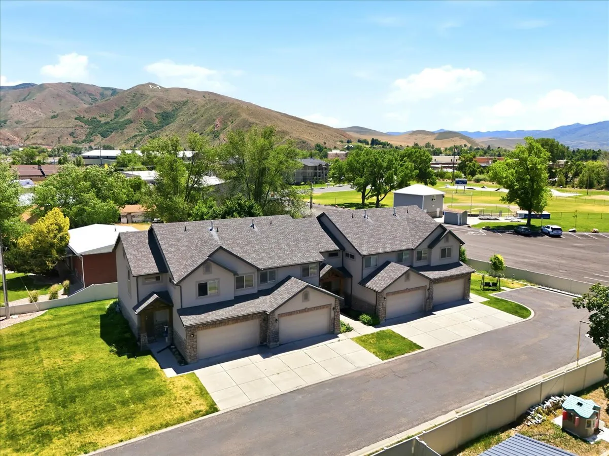 Duplex property featuring a stucco and stone facade, attached garages with sectional doors, concrete driveways, and green lawn areas
