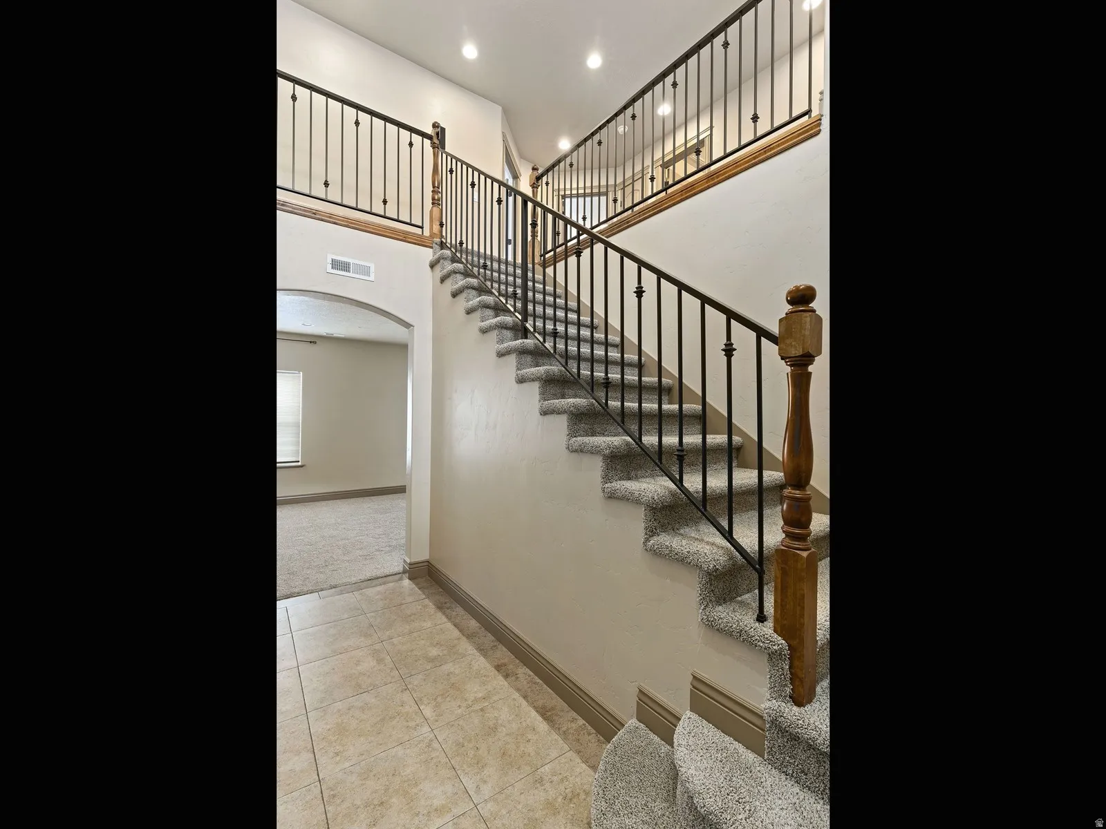 Two-story entryway featuring a carpeted staircase with wrought iron balusters and a wood handrail