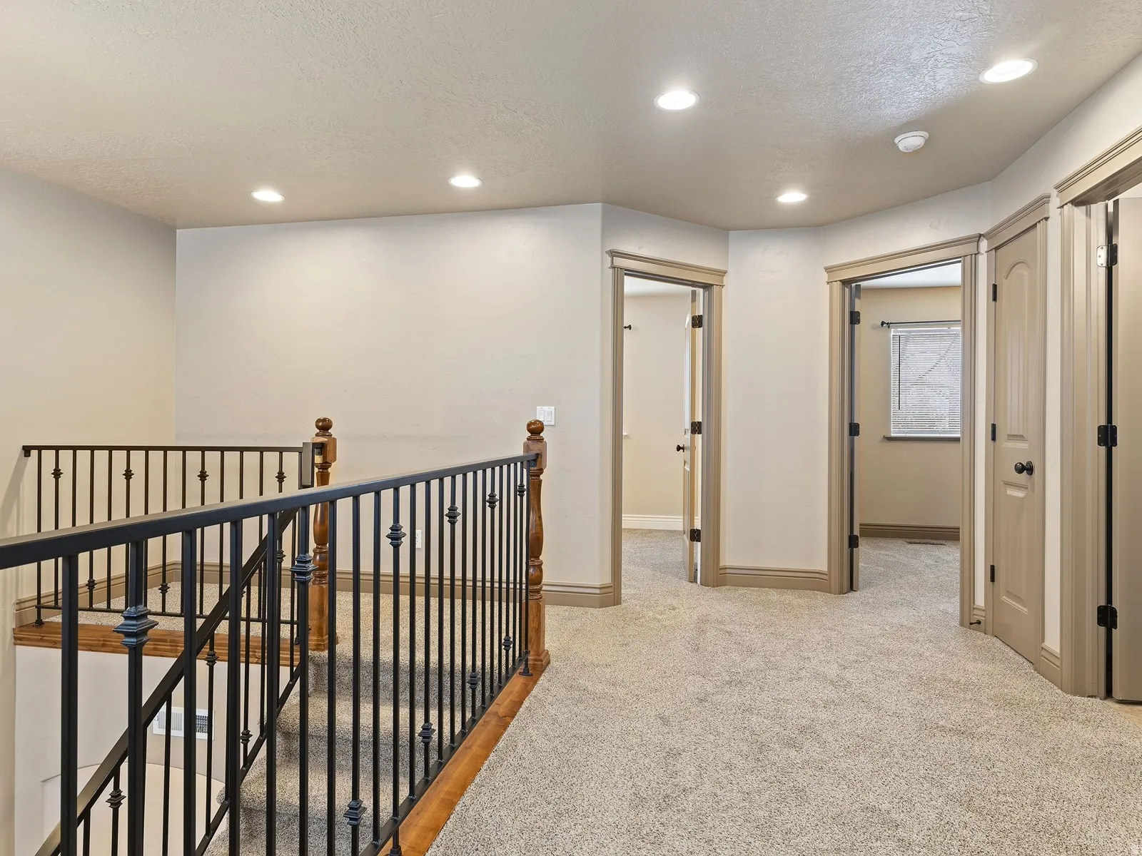 Upper-level hallway featuring plush carpeting, recessed lighting, and a wrought iron and wood banister