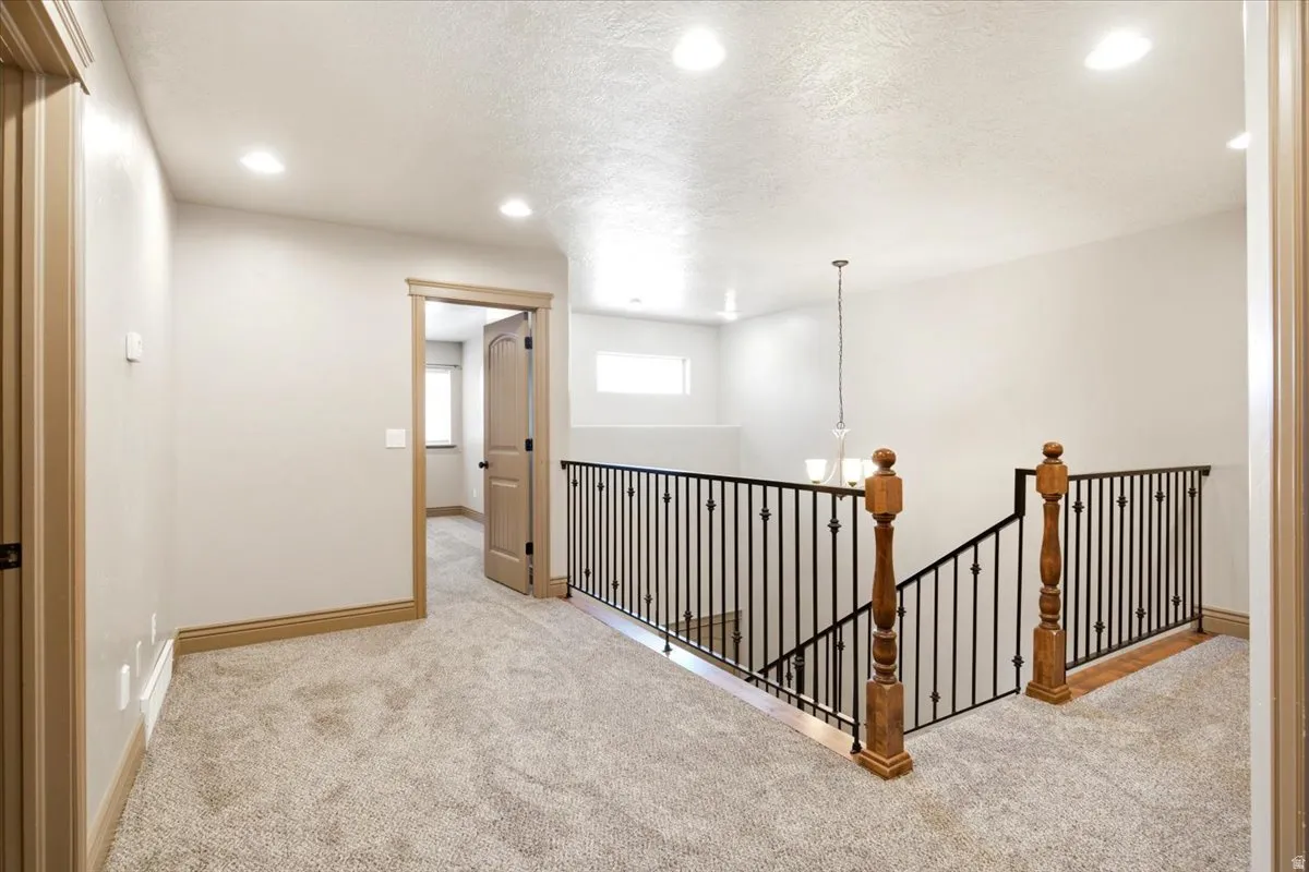 Carpeted upper-level landing featuring recessed lighting and a wrought iron and wood balustrade