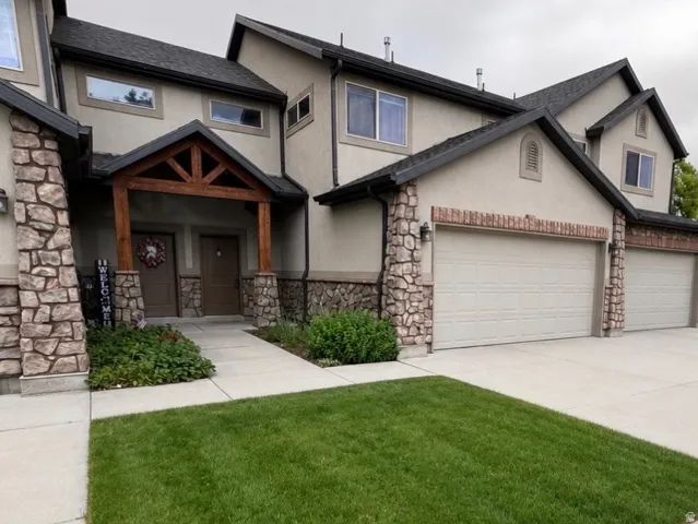 Stucco exterior featuring stacked stone accents, dark trim, and a prominent wood-beam entry