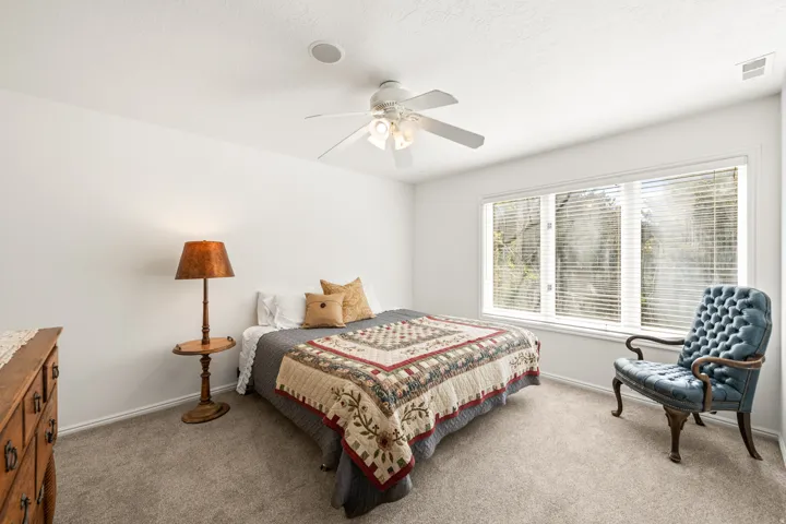 Carpeted bedroom with a large window featuring blinds, a ceiling fan, and white baseboards