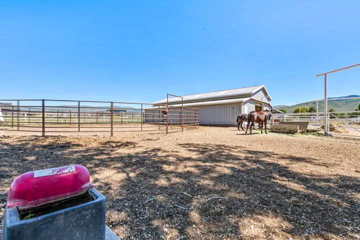 Expansive outdoor equestrian area featuring multiple fenced enclosures, a large barn, and feeding troughs