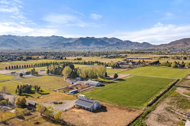 Expansive property featuring a single-story residence, multiple outbuildings, fenced paddocks, and substantial green acreage set against a mountainous backdrop