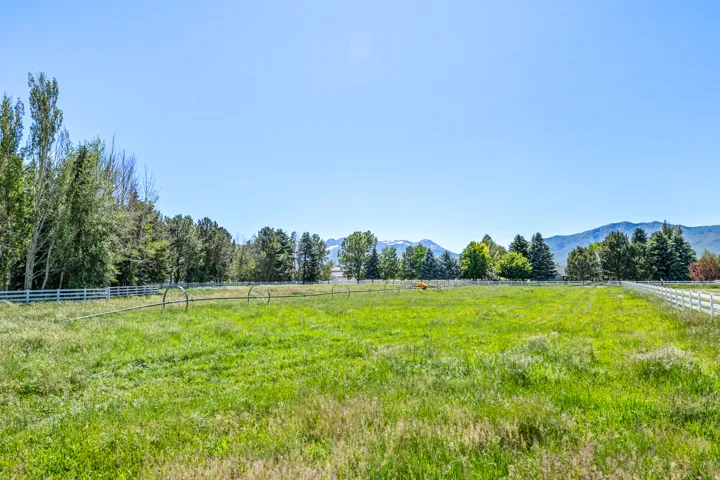 Expansive green field featuring a white perimeter fence, mature trees, and distant mountains