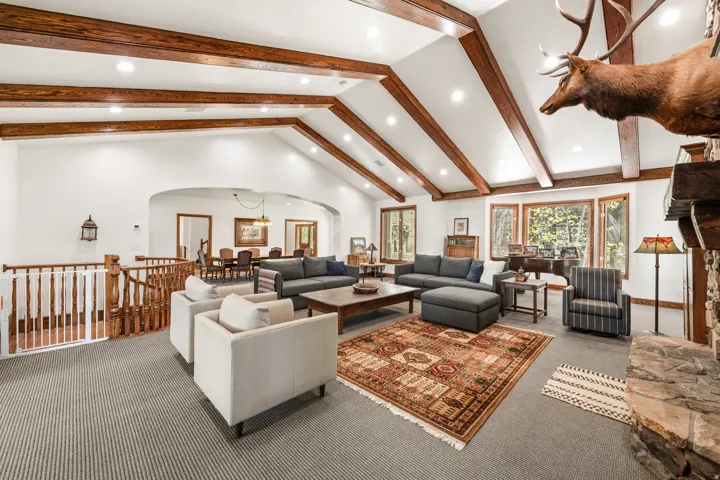 Spacious living area featuring a vaulted ceiling with exposed wood beams, recessed lighting, and a stone-clad fireplace
