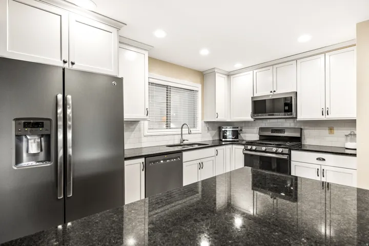 Modern kitchen featuring a large black countertop island, white shaker-style cabinetry, stainless steel appliances, subway tile backsplash, and recessed lighting