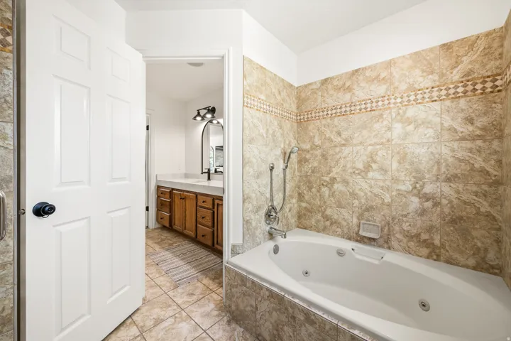 Tiled bathroom featuring a built-in jetted tub, wall-mounted showerhead, and decorative tile accent band