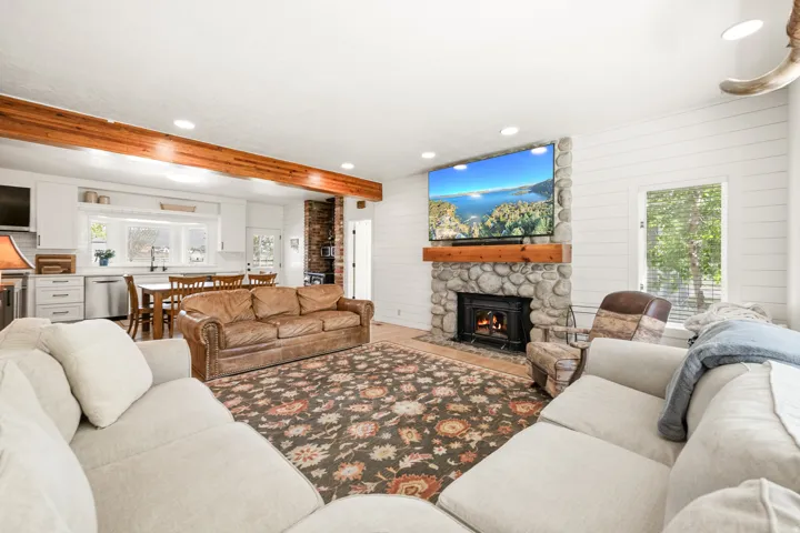 Open concept living space featuring a stone fireplace with wood mantel, wood beam accents, and shiplap wall finishes