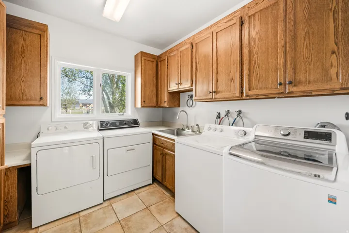 Laundry room featuring a window, tan floor tiling, wood cabinetry, and a utility sink